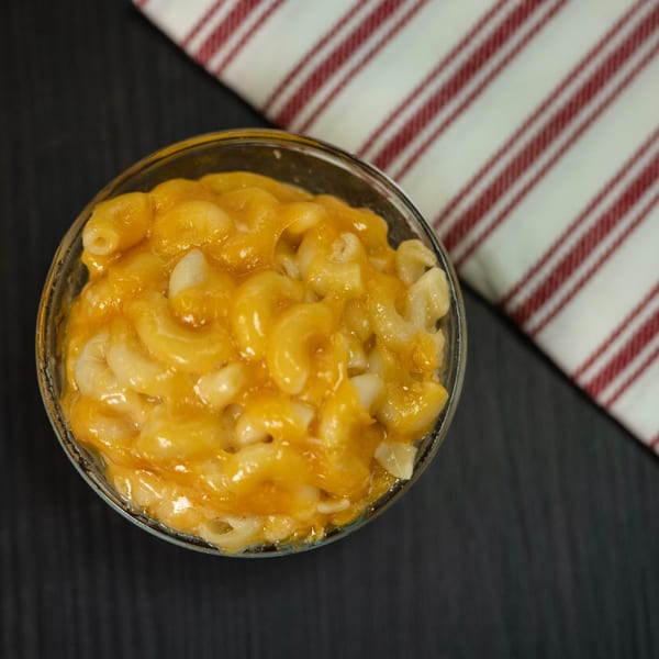 A close-up, overhead view of a glass bowl filled with creamy, golden macaroni and cheese.