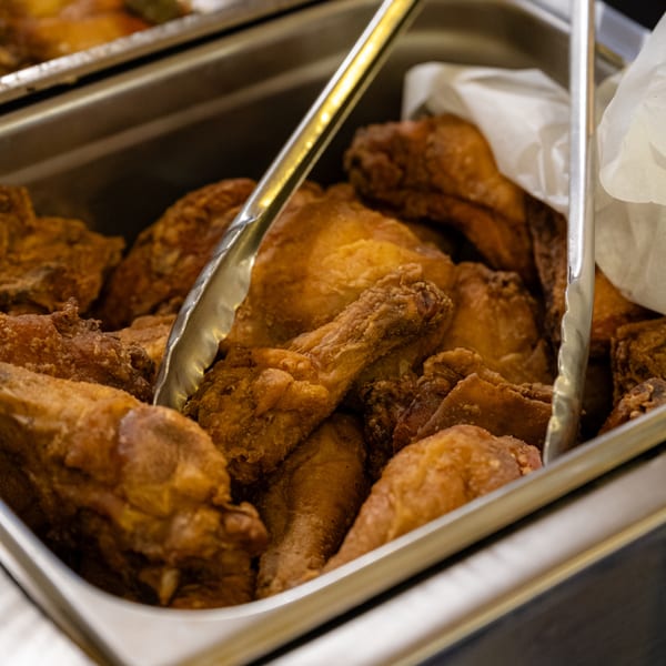 Golden-brown fried chicken pieces in a metal serving tray with tongs, ready to be served.