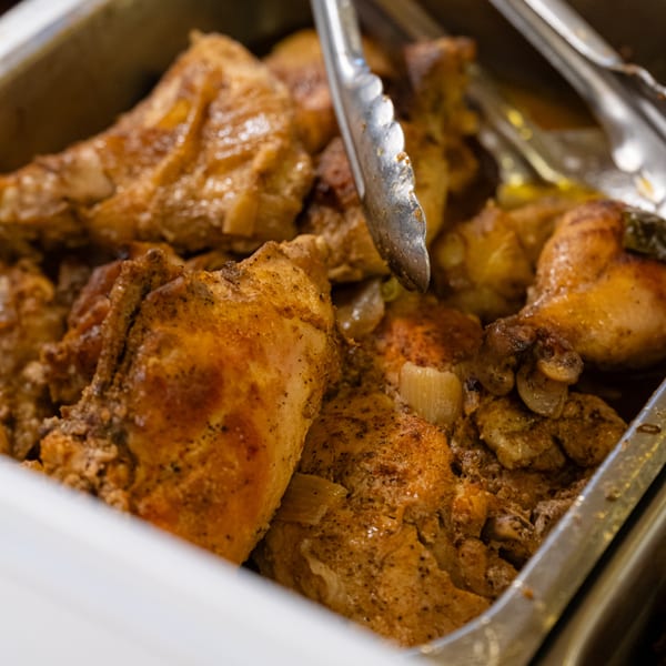 Close-up of golden-brown baked chicken pieces with onions in a metal serving tray at Detroit Soul.