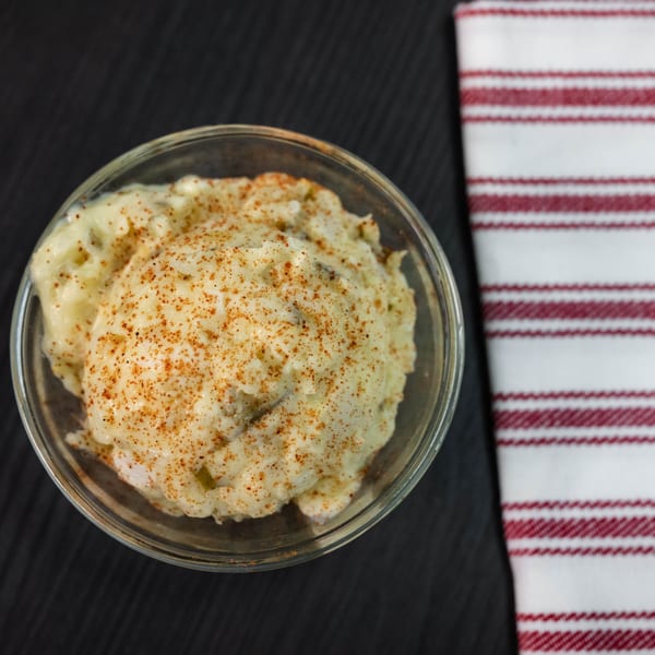 Creamy mashed potatoes with spices in a clear bowl next to a red and white striped napkin.